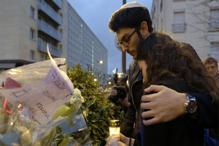 People hold a candle next to flowers during a gathering at the end of Shabbat called by the Jewish Student's Union of France (UEJF) association on Jan. 10, 2015, at the Porte de Vincennes in eastern Paris. (AFP)